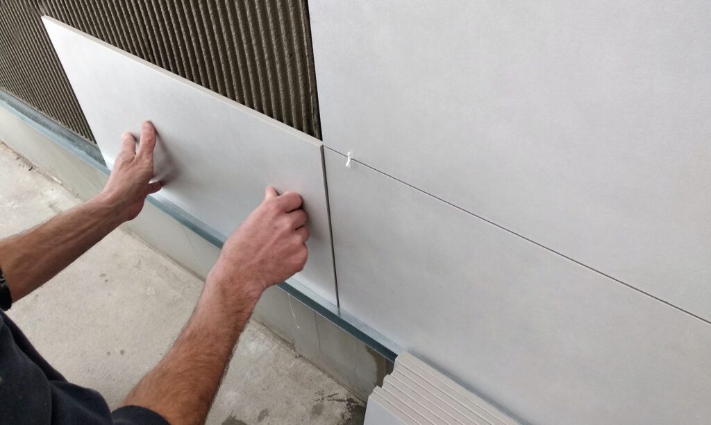 Worker hands putting ceramic tiles on the wall.